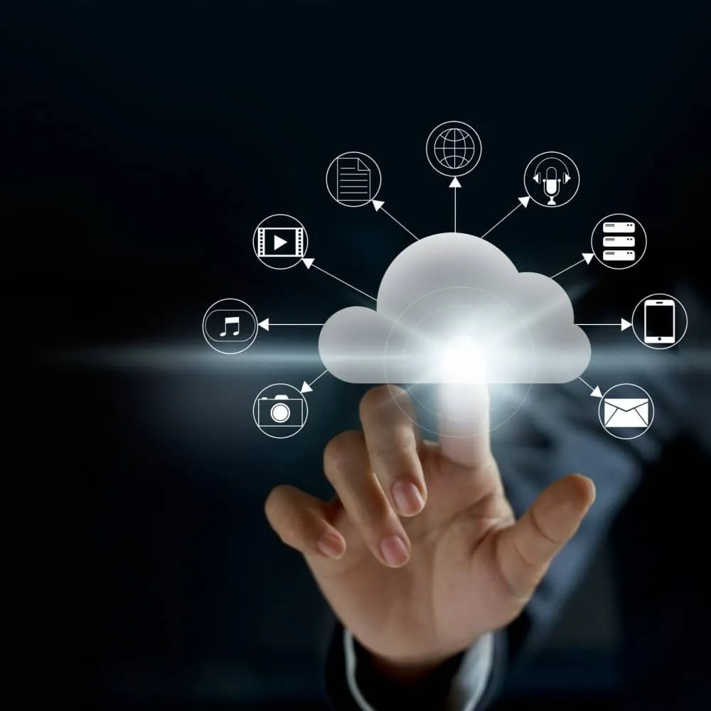 A hand interacts with a cloud icon, surrounded by symbols representing various digital services such as files, music, video, email, and mobile apps—much like selecting a managed hosting service for business solutions—set against a dark background.