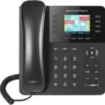 A black office desk telephone with a digital display, keypad, and corded handset. The screen showcases various colorful icons and call information. Designed for VoIP, the phone features several function buttons near the display for enhanced connectivity and communication.